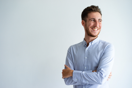 Cheerful businessman enjoying success. Young man in office shirt folding arms, looking away and smiling. Business success concept