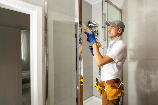 Técnico de mantenimiento hotelero realizando reparación de puerta de ducha en habitación de hotel moderno