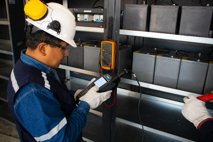 Técnico especializado realizando mediciones eléctricas con multímetro en sala de baterías industriales