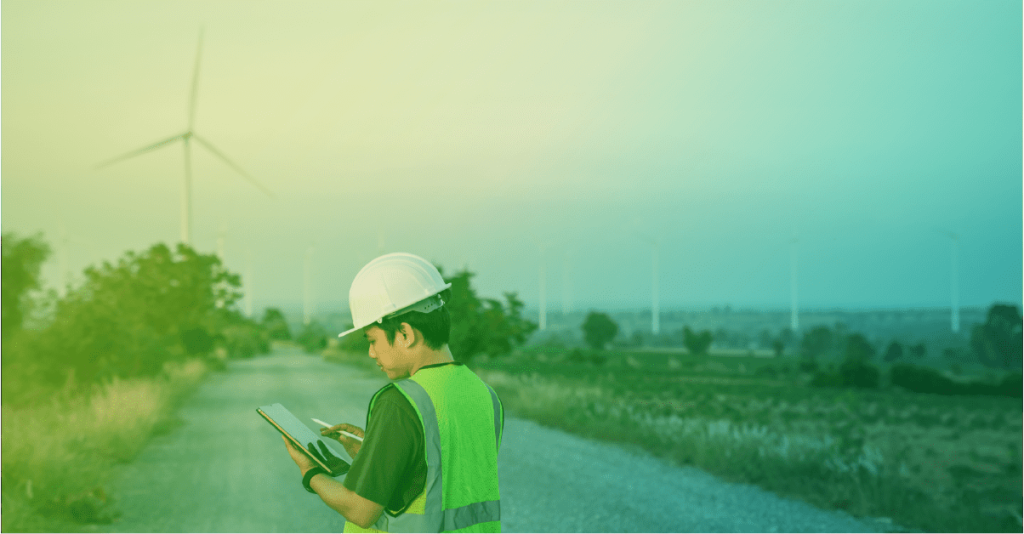Maintenance technician examining work orders on a tablet with CMMShere with a wind turbine in the background